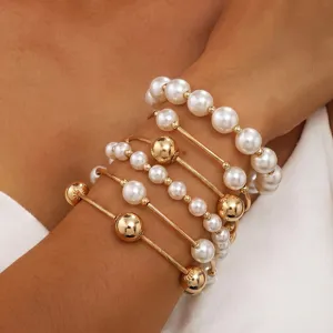 Primer plano de pulseras doradas apiladas y perlas artificiales para la moda femenina cotidiana.
