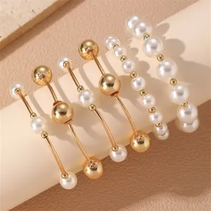 Primer plano detallado del conjunto de pulseras apiladas de metal dorado y perlas falsas.