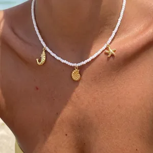 Detailaufnahme einer weißen Rocailles-Halskette mit goldenen Muschel- und Seesternanhängern.