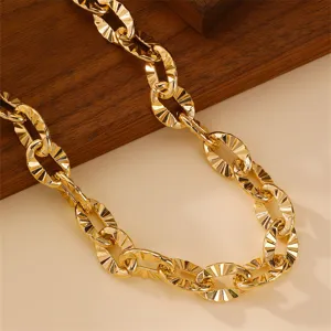 Close-up detail of a bold gold metal chain necklace, featuring striking textured links.