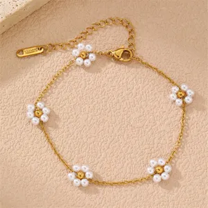 Nahaufnahme Detail des goldenen Armbands mit weißen Perlenblumen Anhängern und Karabiner.