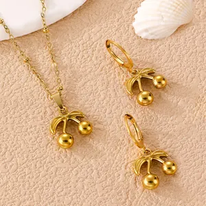 Goldenes Edelstahl Kirsche Schmuckset Detailansicht auf strukturiertem beigen Hintergrund.