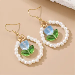 Primer plano de elegantes pendientes de perlas con flor de vidrio azul y ganchos.