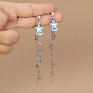 Primo piano di raffinati orecchini pendenti argentati con ciondoli a stella blu e catenine.