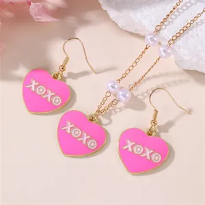 Close-up detail of pink heart enamel necklace and earrings set with sweet XOXO and pearls.