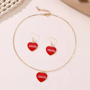 Detail shot of gold chain necklace and earrings set featuring red heart pendants with XOXO print.