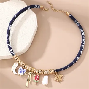 Nahaufnahme einer eleganten Damen-Charm-Halskette mit blauem Stoffband und Goldperlen.