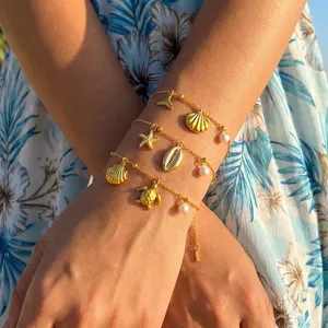 Detailaufnahme mehrlagiger goldener Strand-Armbänder mit Muschel- und Perlen-Anhängern.