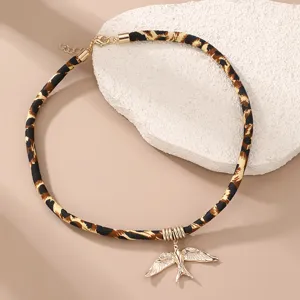 Detailansicht einer kurzen Kette mit Leopardenmuster Stoffkordel und goldenem Schwalben-Anhänger.