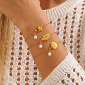 Nahaufnahme Detail des dreilagigen Goldkettenarmbands mit Muschel Perlen Anhängern.