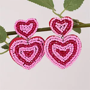 Vista dettagliata di orecchini pendenti a doppio cuore con perline rosa fatte a mano.