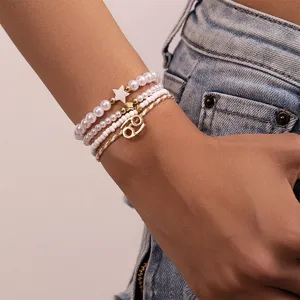 Nahaufnahme eines mehrschichtigen Perlen- und Perlenarmbands mit goldenem Sternzeichen-Anhänger.