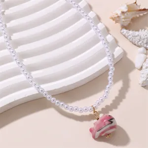 Detailansicht einer eleganten weissen Perlenkette mit einem niedlichen rosa Keramikfisch.