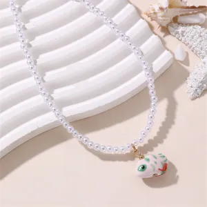 Detaillierte Nahaufnahme der eleganten weißen Perlenkette mit Keramikanhänger auf Muschel.
