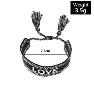 Close-up detail of black and white woven bracelet with LOVE embroidery and tassel ends.