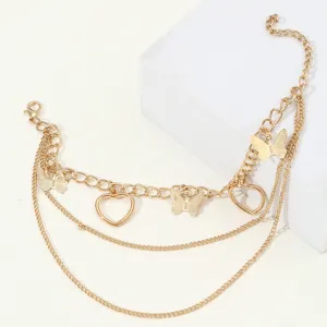 Close-up detail of multi-layer gold butterfly heart charm chain anklet summer jewelry