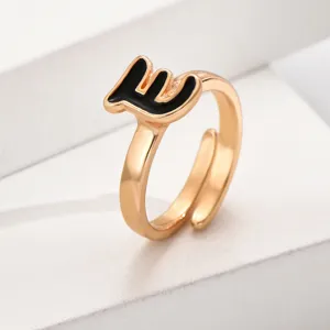 Nahaufnahme eines vergoldeten offenen Rings mit schwarzem Buchstaben, verstellbares Design.