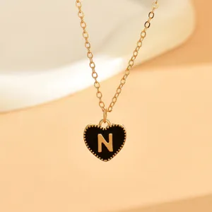 Nahaufnahme einer Goldkette mit einem schwarzen Emaille-Herz-Anhänger und der Letter N.