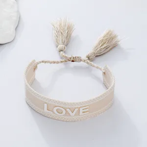 Detail shot of beige woven braided couple bracelet featuring decorative tassels and love lettering.
