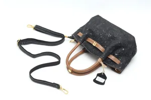 Detail view of black embossed leather vintage handbag with brown handle and strap.