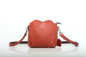 Orange leather crossbody bag detail view, showing pebble grain texture and metal hardware.