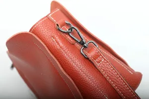 Detail shot of orange leather crossbody bag featuring contrast white stitching and metal hardware.