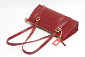 Red leather shoulder bag detail showing genuine leather texture, metal buckles and double straps.