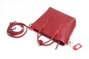 Red leather handbag detail showcasing fine texture, dual handles and detachable strap.