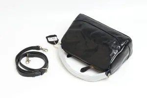 Black genuine leather Boston handbag detail showing texture, strap and attached product tag.