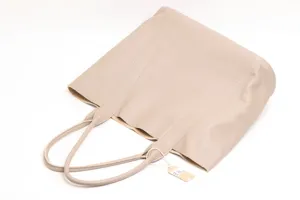 Detail view of a minimalist beige leather tote bag with dual handles and hanging tag.