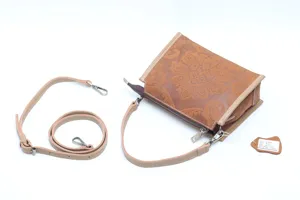 Detailed view of brown embossed leather handbag with floral pattern, zipper and strap.