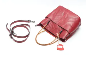 Detailed view of genuine leather red bucket bag with brown handles and adjustable strap.