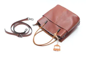 Close up of a brown leather bucket bag detail showing top handle, texture and strap.