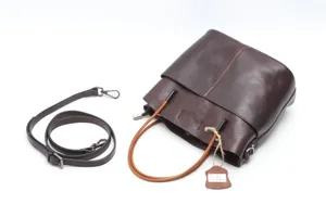 Detail shot of the brown leather bucket bag showing its texture, handles, and hanging tag.