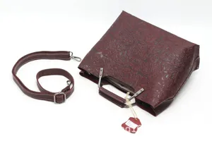 Detailed view of dark red embossed leather handbag, retro floral design with metal frame.