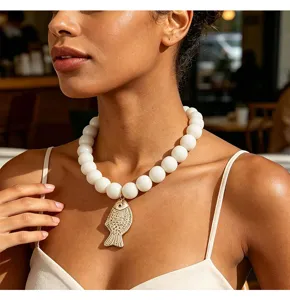Détail en gros plan du collier de perles blanches élégantes avec un pendentif poisson doré.