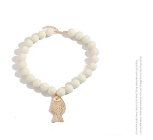 Vue détaillée du pendentif poisson doré et du collier de perles blanches, bijou chic.