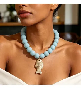 Gros plan détaillé du collier de perles bleu clair élégant avec un pendentif poisson doré.