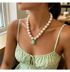 Primo piano di una grossa collana di perle bianche con ciondolo a borsa in giada verde.