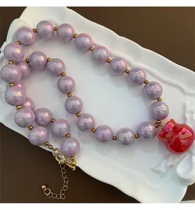 Primo piano dettagliato della collana di perle acriliche iridescenti viola con ciondolo.