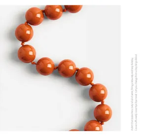 Close-up detail shot of glossy orange acrylic round beads necklace, minimalist white style.