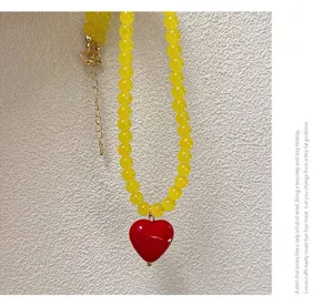 Vue détaillée du collier de perles jaunes avec pendentif cœur rouge, accessoire.
