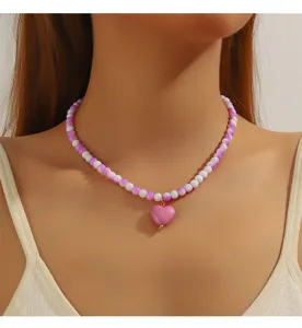 Gros plan détaillé du collier de perles tendance avec pendentif cœur rose au cou.