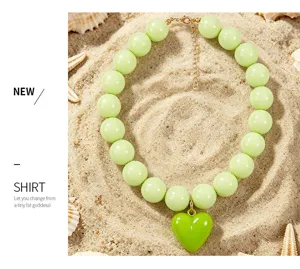 Gros plan détaillé d'un collier de perles en acrylique vert clair avec pendentif cœur sur le sable.