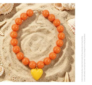 Gros-plan d'un collier de perles en acrylique orange bohème avec pendentif cœur.