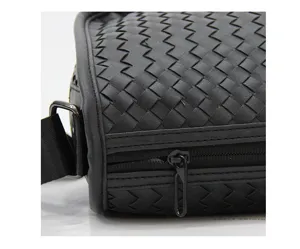 Close-up view of black woven leather messenger bag detail, featuring exquisite intrecciato pattern.
