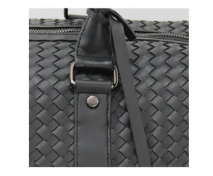 Close-up of black woven leather travel bag detail showing premium texture and hardware.