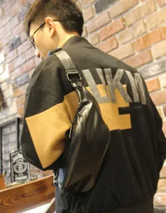 Detail shot of stylish black leather chest bag worn across the back, showing sleek zipper design.