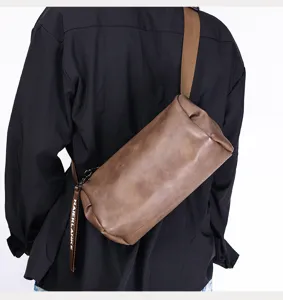 Detail shot of a stylish brown cylindrical crossbody bag worn by a man, showing strap and design.