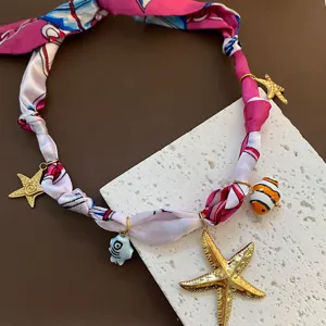 Detailaufnahme der süßen maritimen Charm-Stoffbandkette mit Seestern- und Fischanhängern.